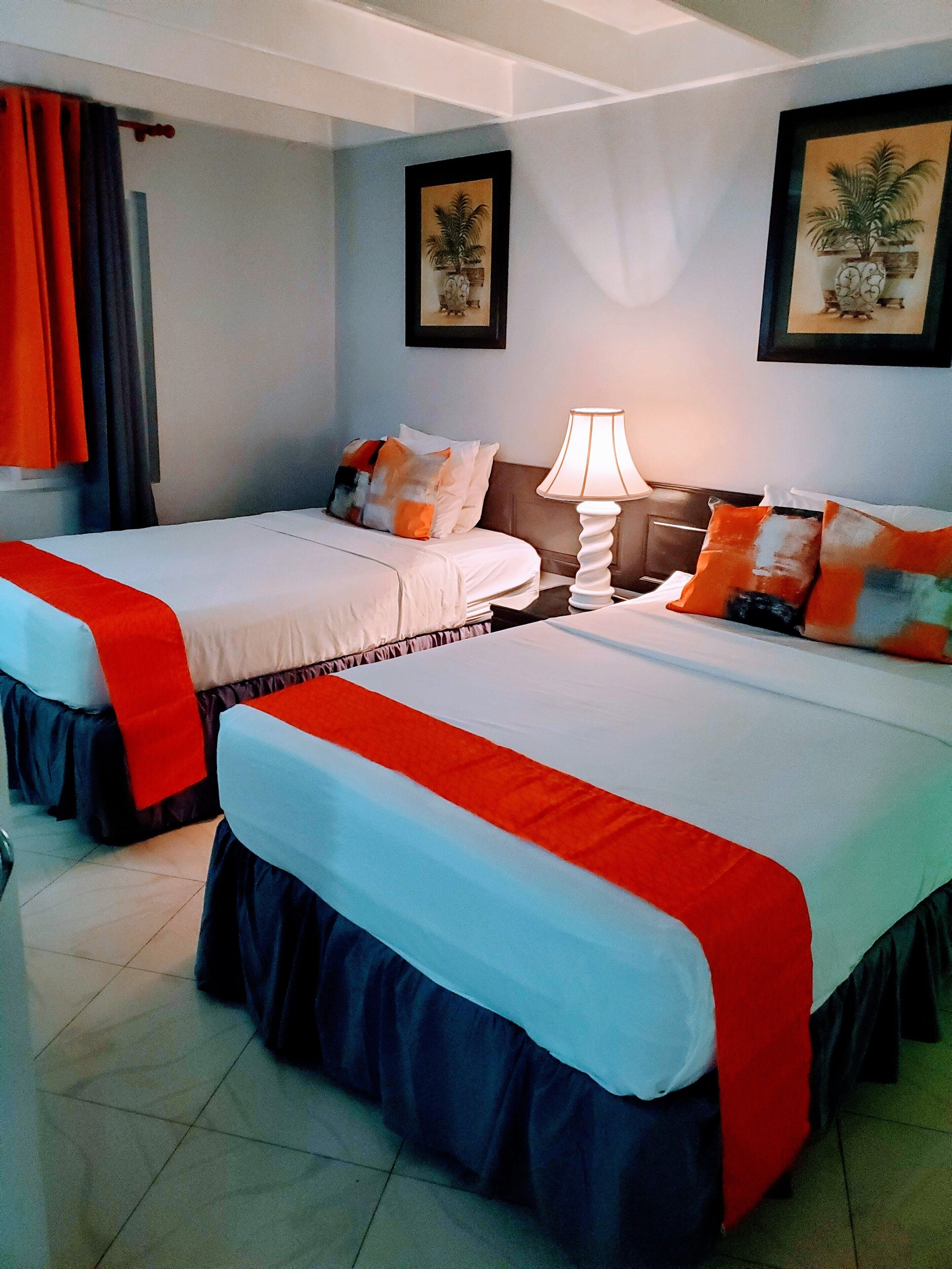 A hotel room with two beds, each with a red and white bedspread, a nightstand with a lamp, and two framed pictures on the wall.