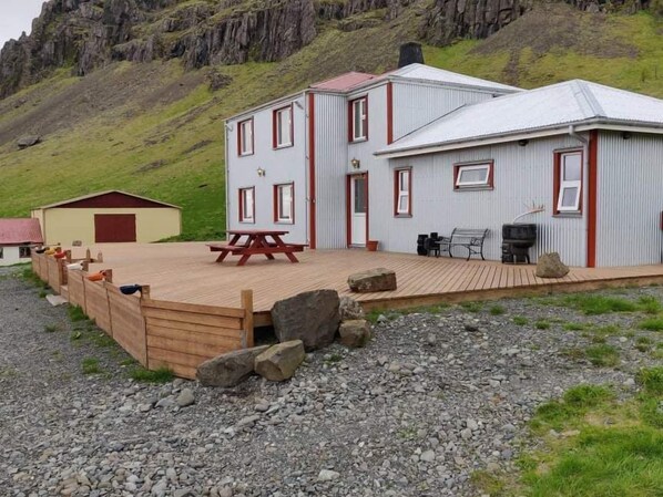 A rustic cabin with a wooden deck, a picnic table, and a barbecue area.