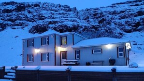 A two-story building with a snow-covered roof and a wooden deck in front. - Guesthouse Stekkatún (Höfn)