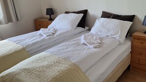 A double bed with white linens, two bedside tables with lamps, and a wooden nightstand with a lamp. - Guesthouse Stekkatún (Höfn)