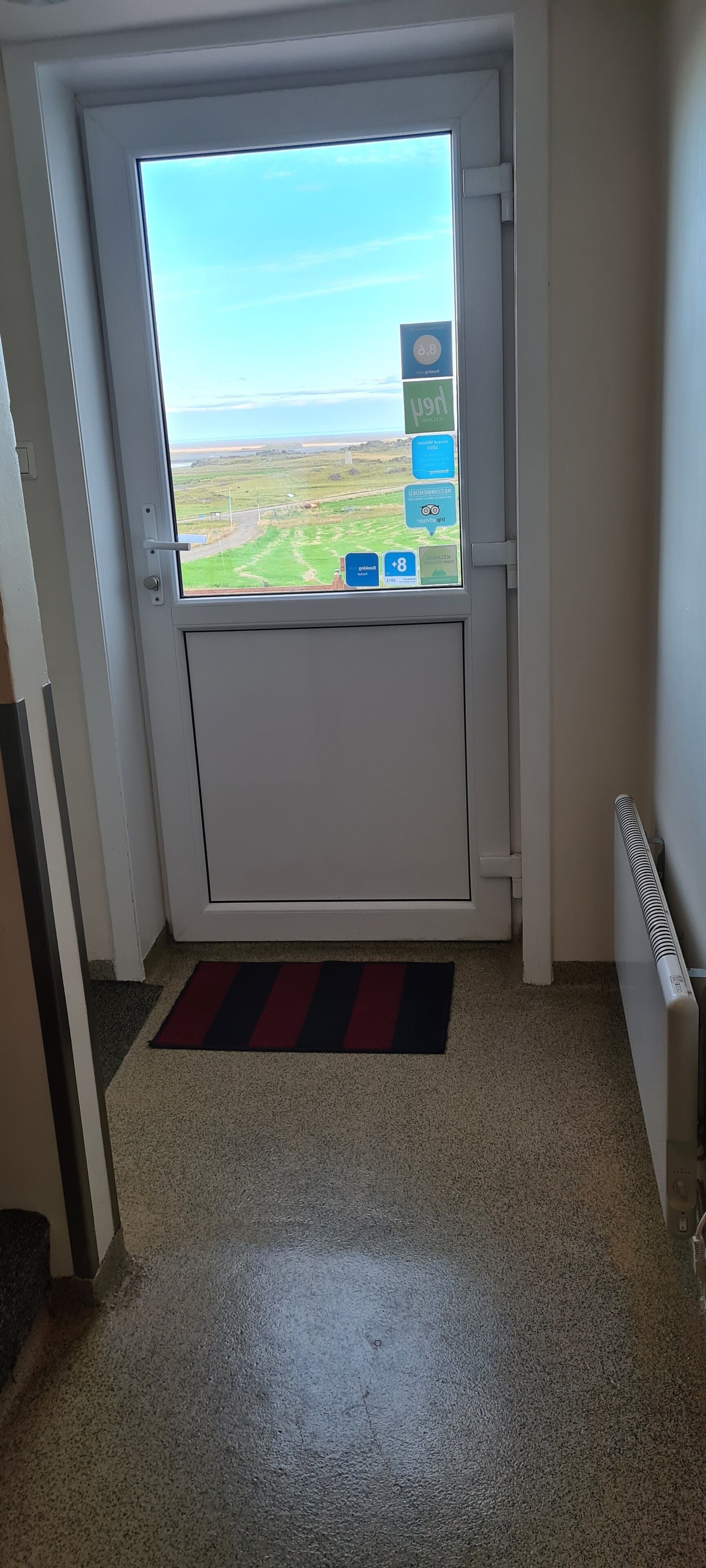 A door with a view of a green landscape through a window, a red and black striped mat, and a white radiator.