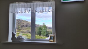 A window with a white curtain, a white cat figurine, and a small picture frame on a white shelf. - Guesthouse Stekkatún (Höfn)