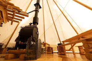 Interior de una carpa con estufa de leña, bancos de madera y contenedores de almacenamiento.