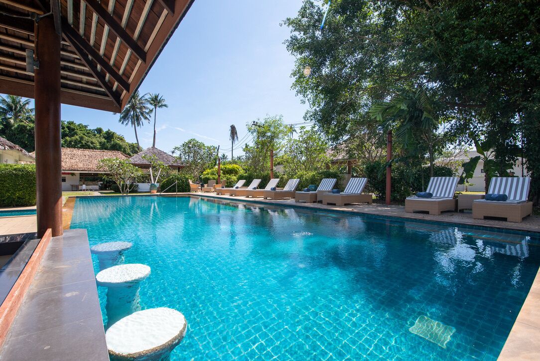 A clear blue swimming pool with lounge chairs and a covered area.