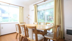 A dining area with a wooden table and chairs, large windows with curtains, and a wall-mounted air conditioner. - Sumi Villa Hakuba (Hakuba)