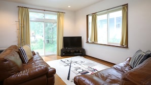 A living room with a brown leather sofa, a flat-screen TV on a stand, and a patterned rug. - Sumi Villa Hakuba (Hakuba)