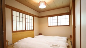 A traditional Japanese-style room with tatami flooring, a wooden headboard, and large shoji screens. - Sumi Villa Hakuba (Hakuba)