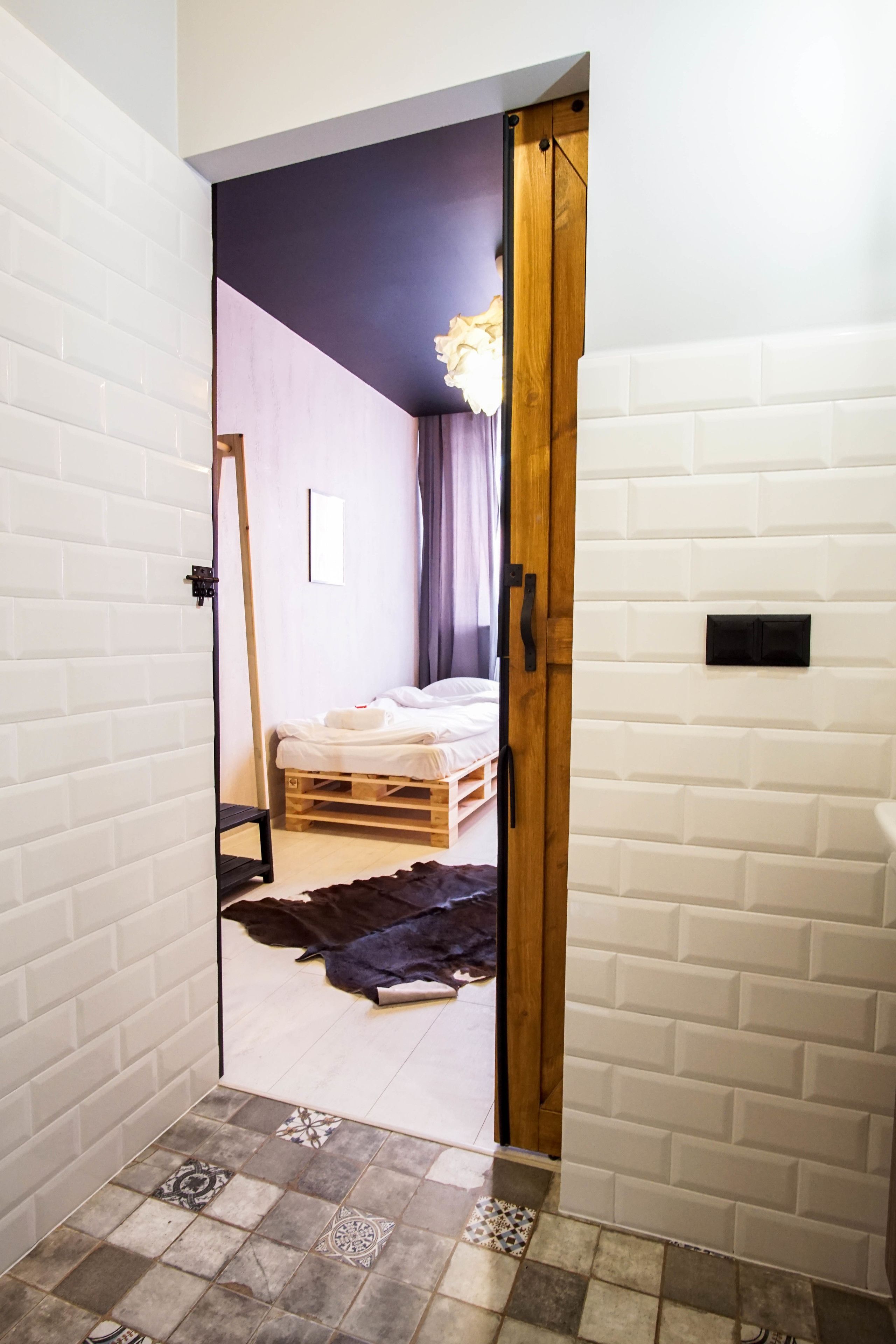 Un couloir étroit mène à une chambre qui contient un lit, une porte en bois et un miroir.
