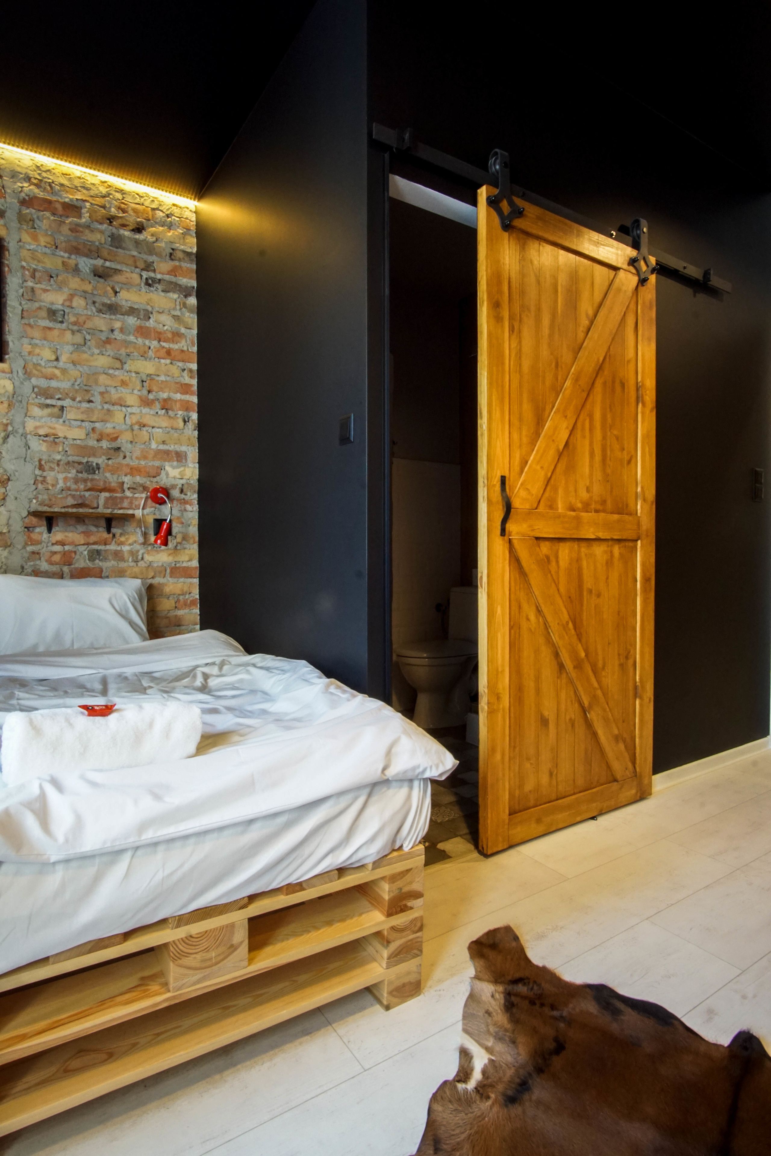 Une chambre avec un lit en bois, un mur en briques, une porte coulissante de style grange et un tapis en peau de vache.