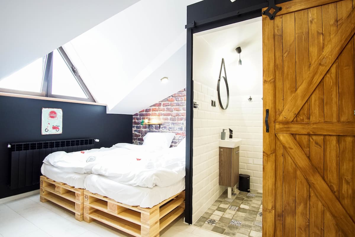 A bedroom with a loft-style ceiling, a wooden bed, a brick wall, a white radiator, and a wooden door.