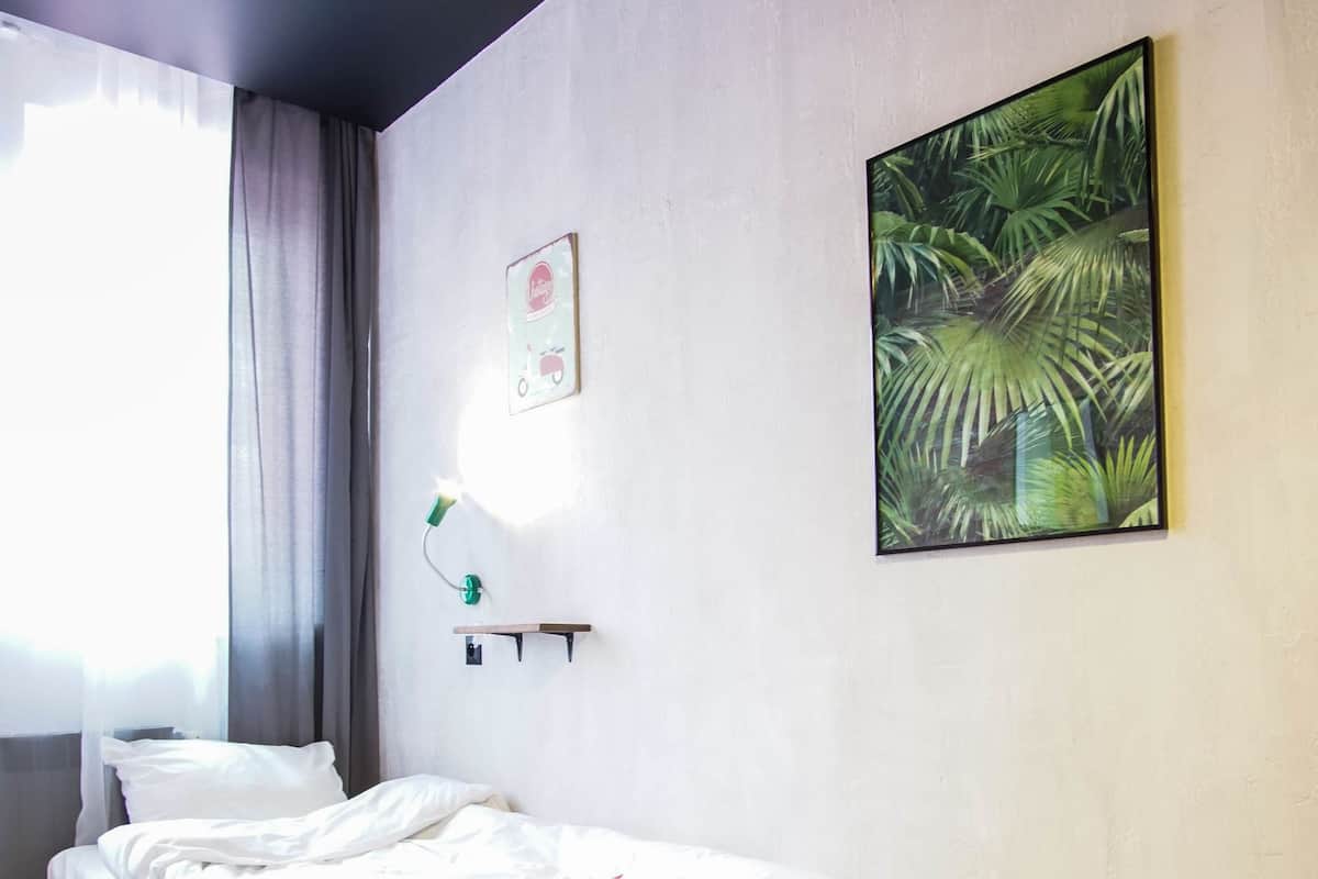 A room with a bed on a wooden pallet, a wall-mounted light, a framed picture, and a window with curtains.