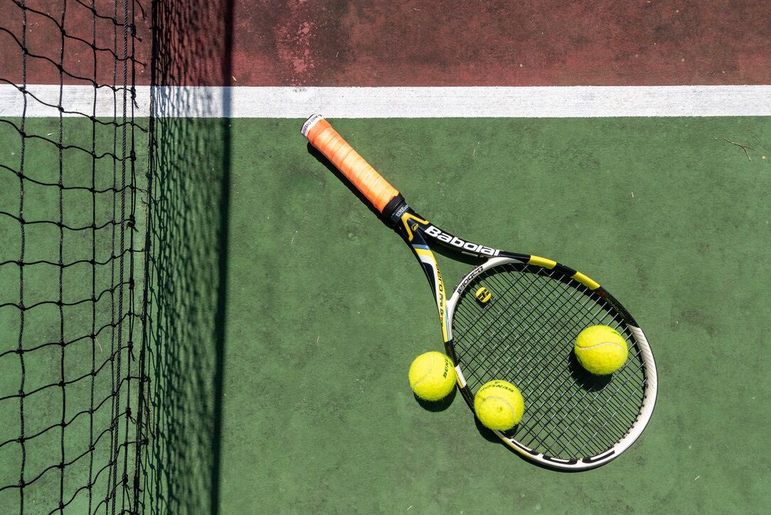 A tennis court with a net, a tennis racket, and three tennis balls.