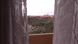 Udsigt fra en balkon med mønstrede gardiner, over en by med bygninger og en bakke.