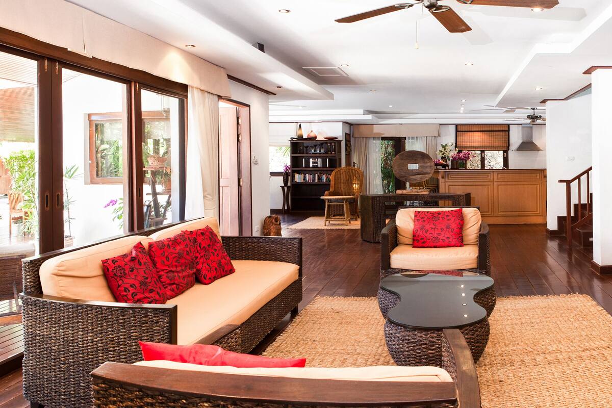 A spacious living area with a sofa, a coffee table, and a dining table. There is a bookshelf and a painting on the wall.