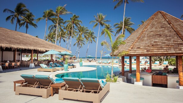 A resort pool area with lounge chairs, umbrellas, and a thatched-roof structure. - Baan Astasia (Koh Samui)