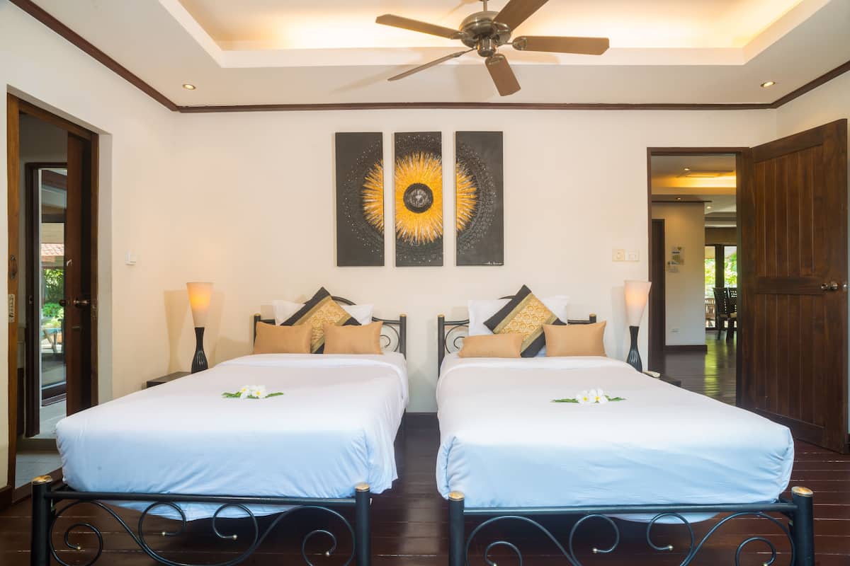 A hotel room with two beds, a ceiling fan, and artwork on the wall.