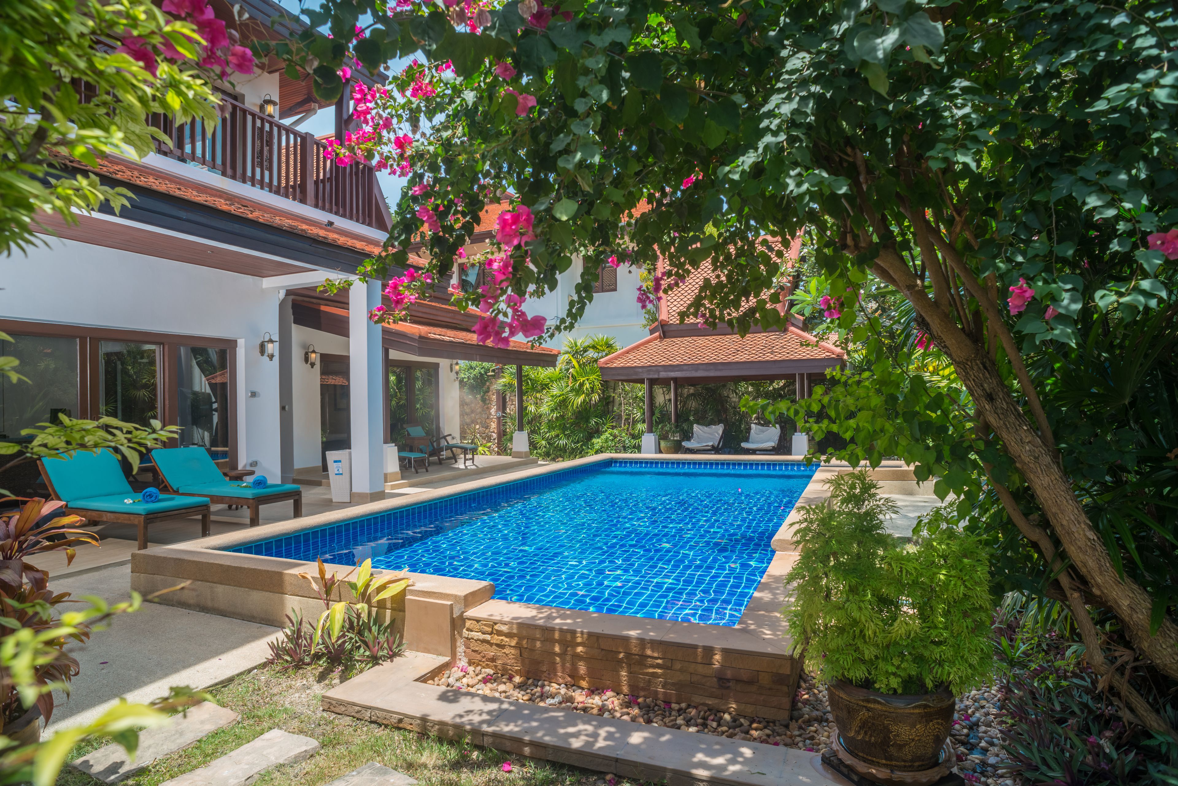 A swimming pool surrounded by lush greenery and a white building with a balcony.