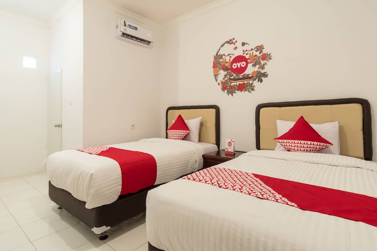 A hotel room with two beds, each with a red and white bedspread and matching pillows. There is a wall decoration with the word "OYO" and a floral design.