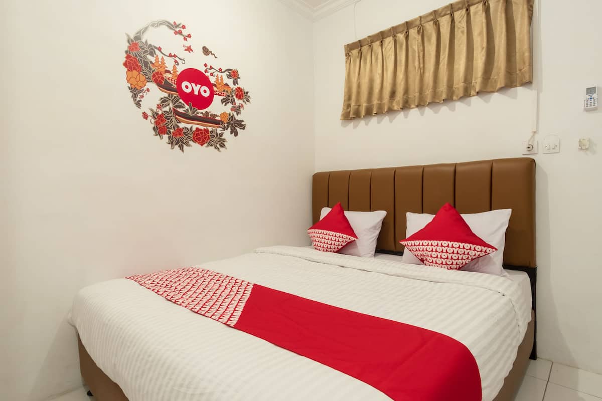 A neatly made bed with a red and white bedspread, two pillows with red and white patterns, and a wall decoration with a red circle and floral design.