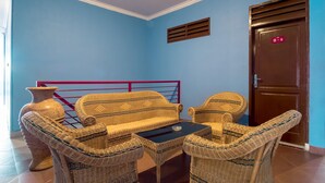A room with a blue wall, wicker furniture, a small table, a door with a sign, and a window with a curtain. - Hotel O Titipapan Residence (Medan)
