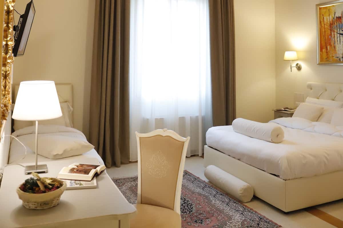 Habitación de hotel con cama, escritorio con lámpara, silla, mesa de comedor con un tazón y ventana con cortinas.