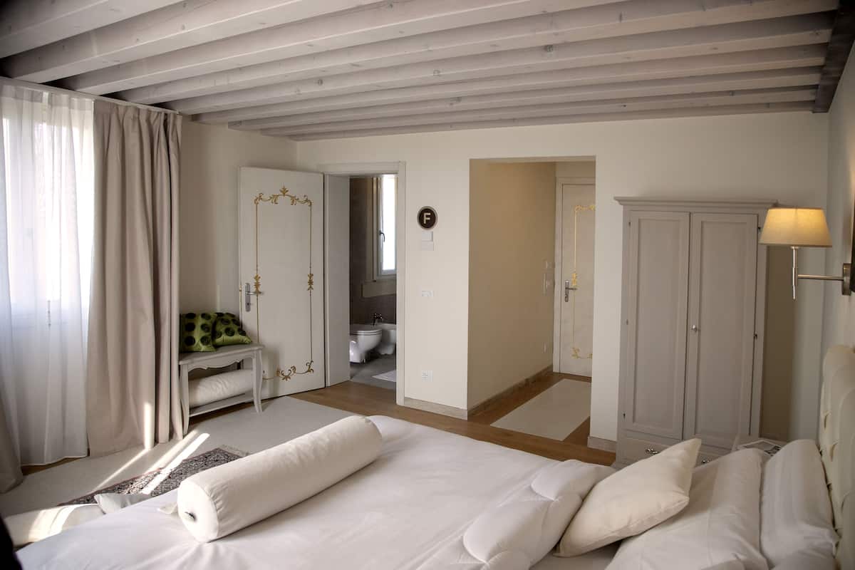 Un dormitorio con una cama grande, una mesita de noche, un armario y un baño visible a través de una puerta abierta.
