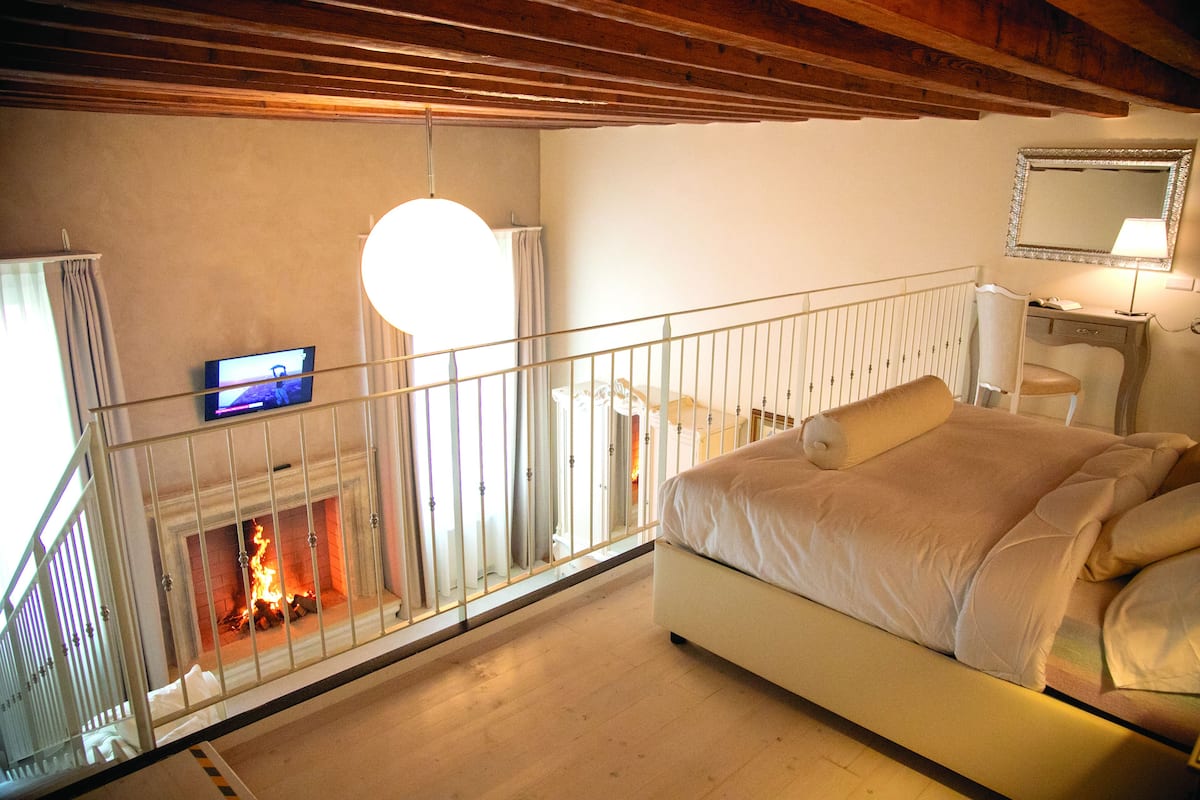 Un dormitorio con cama, chimenea, televisor y barandilla de balcón.
