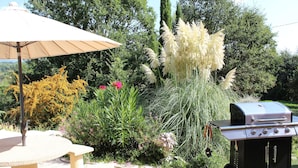 A patio with a stone table, an umbrella, and a portable grill. - Villa Colibri (Lorgues)