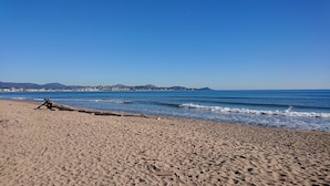 A wide sandy beach with gentle waves, a clear blue sky, and distant mountains. - Villa Colibri (Lorgues)