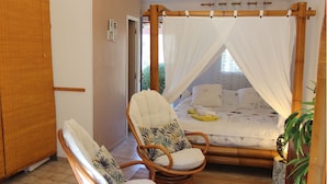 A room with a bed under a canopy, a chair with a cushion, and a bedside table. - Villa Colibri (Lorgues)