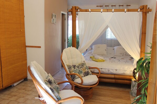 A room with a bed under a canopy, a chair with a cushion, and a bedside table. - Villa Colibri (Lorgues)