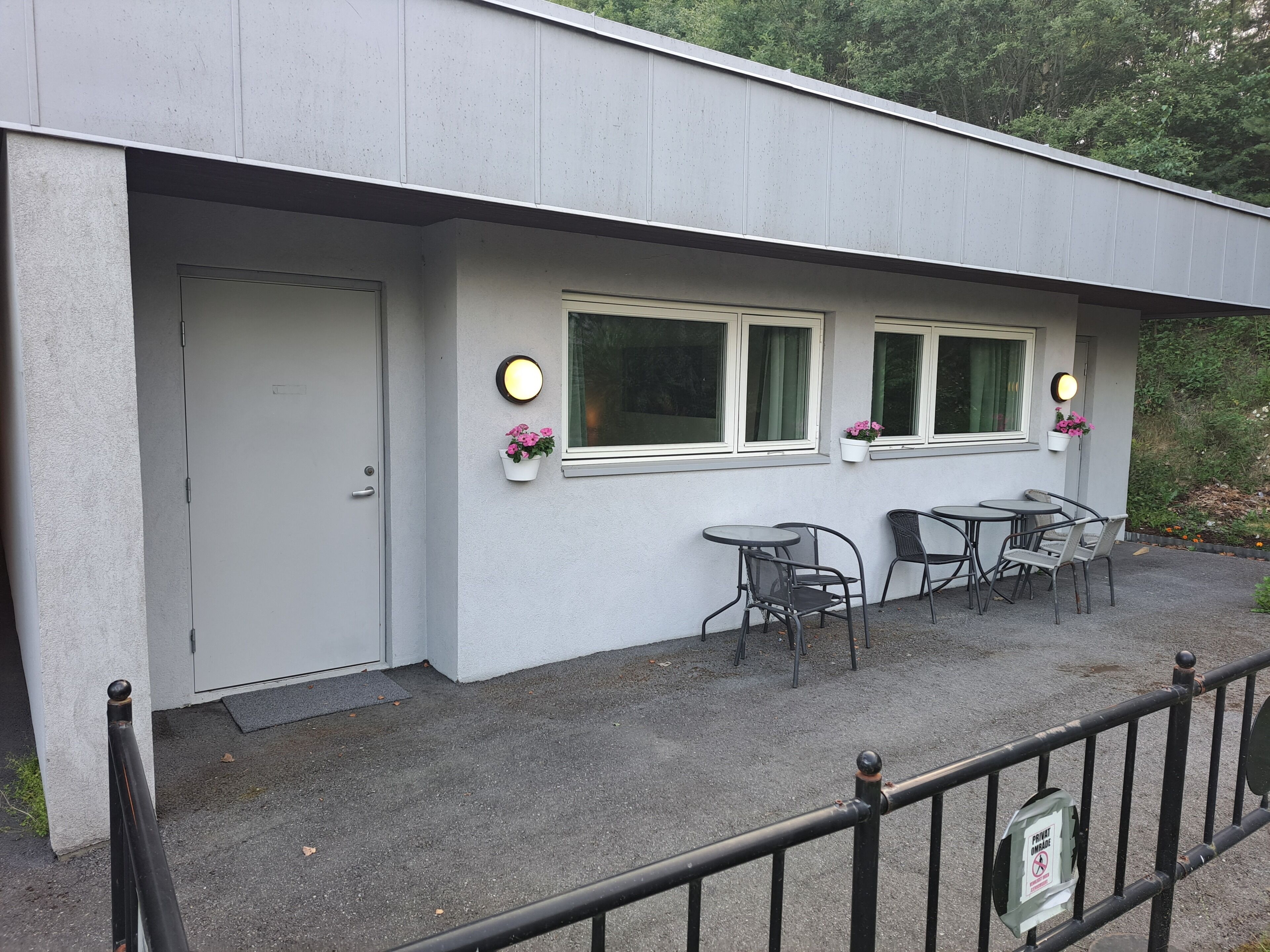A building with a white exterior, a door, and two windows with flower boxes. There are two tables and four chairs outside.