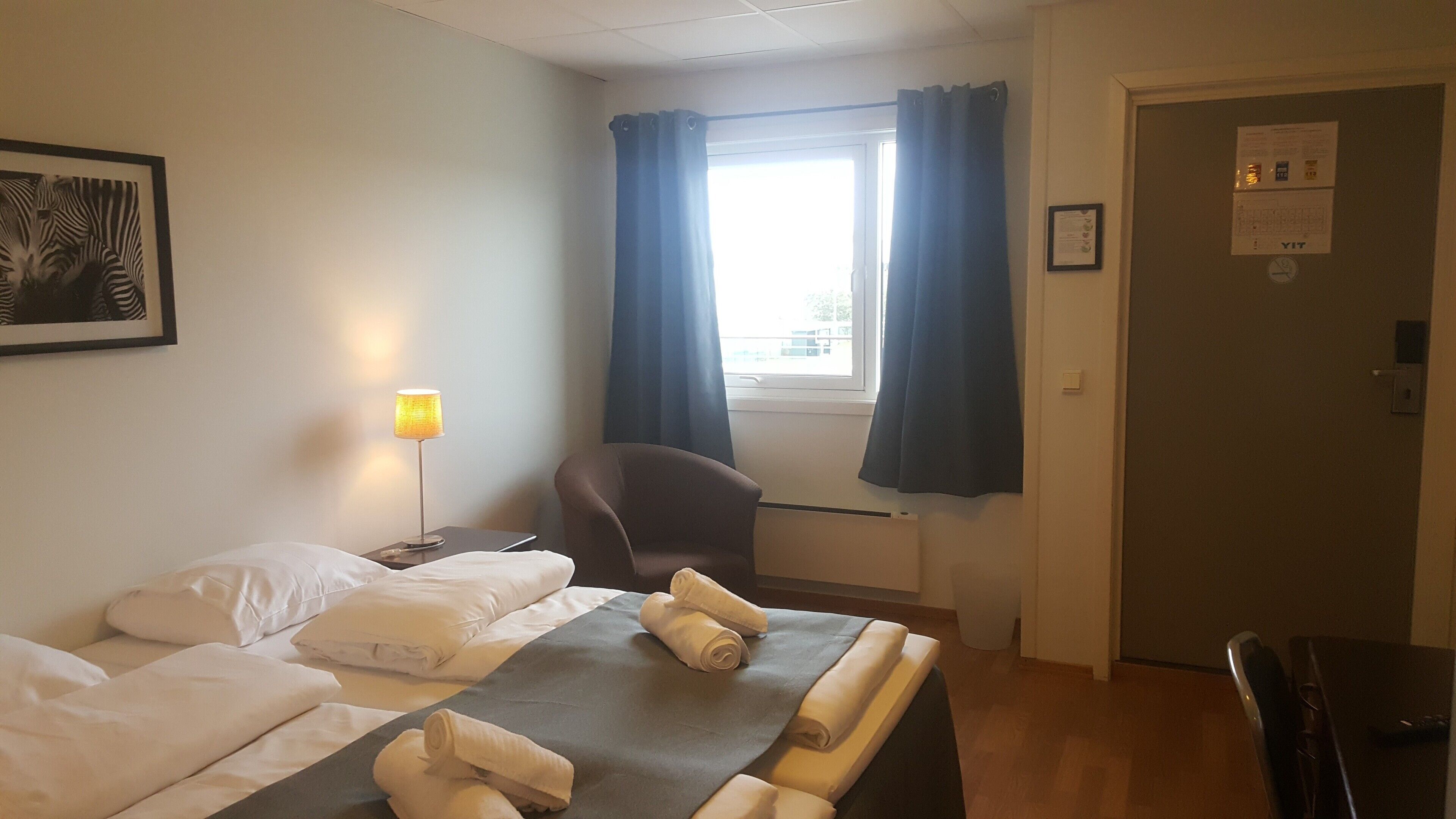 A hotel room with two beds, a desk, a chair, a lamp, and a window with curtains.