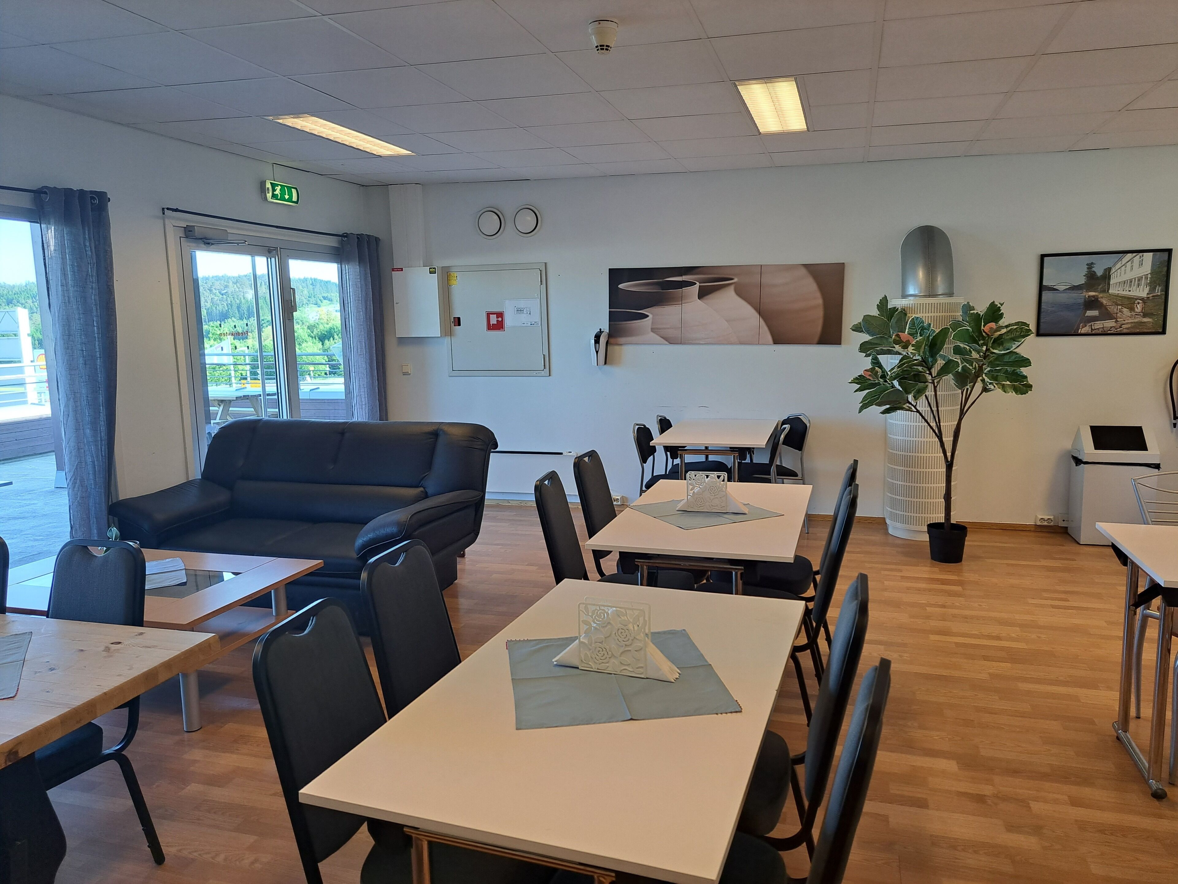 A conference room with a black leather sofa, multiple tables with chairs, a potted plant, and a painting on the wall.