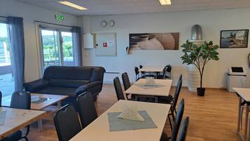 A conference room with a black leather sofa, multiple tables with chairs, a potted plant, and a painting on the wall.