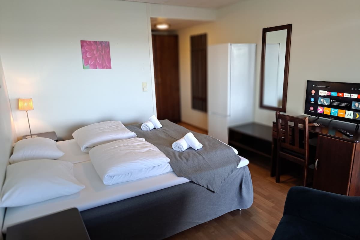 A hotel room with a bed, a desk, a chair, a television, and a door.