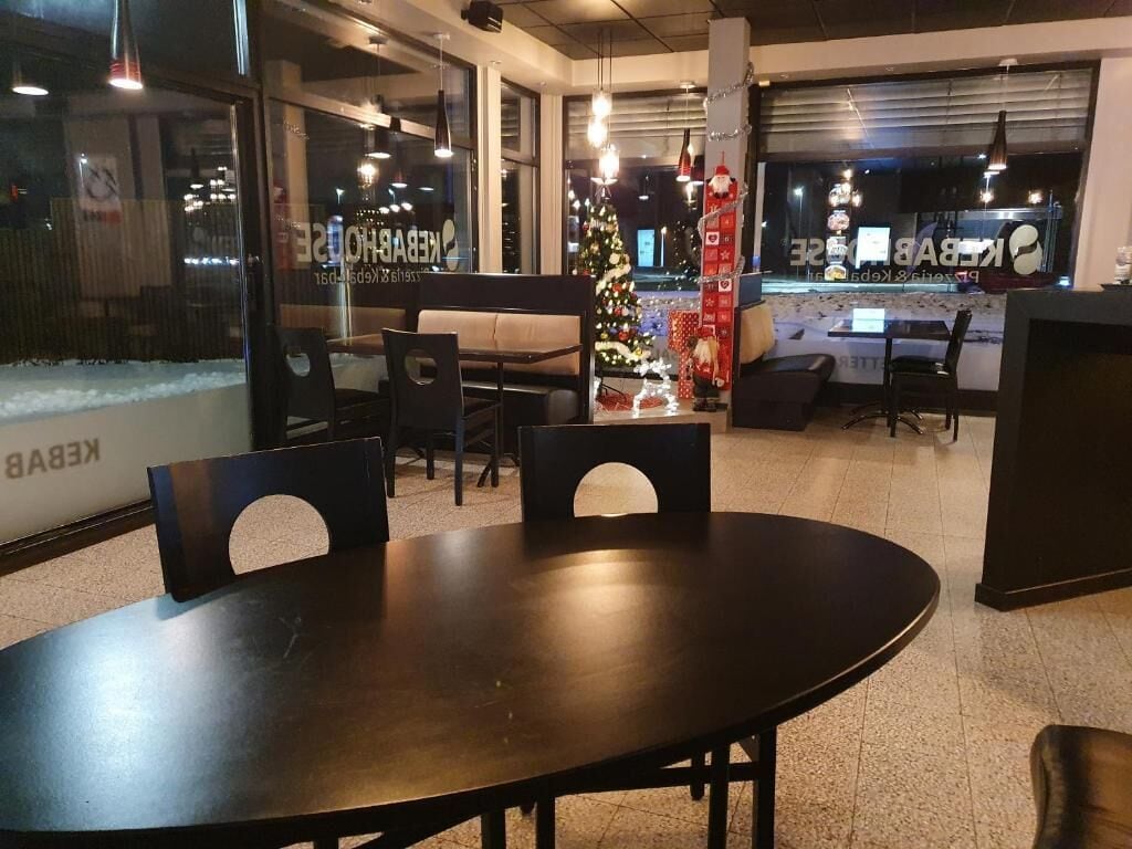 A restaurant interior with a round table, chairs, a Christmas tree, and a counter with a menu display.