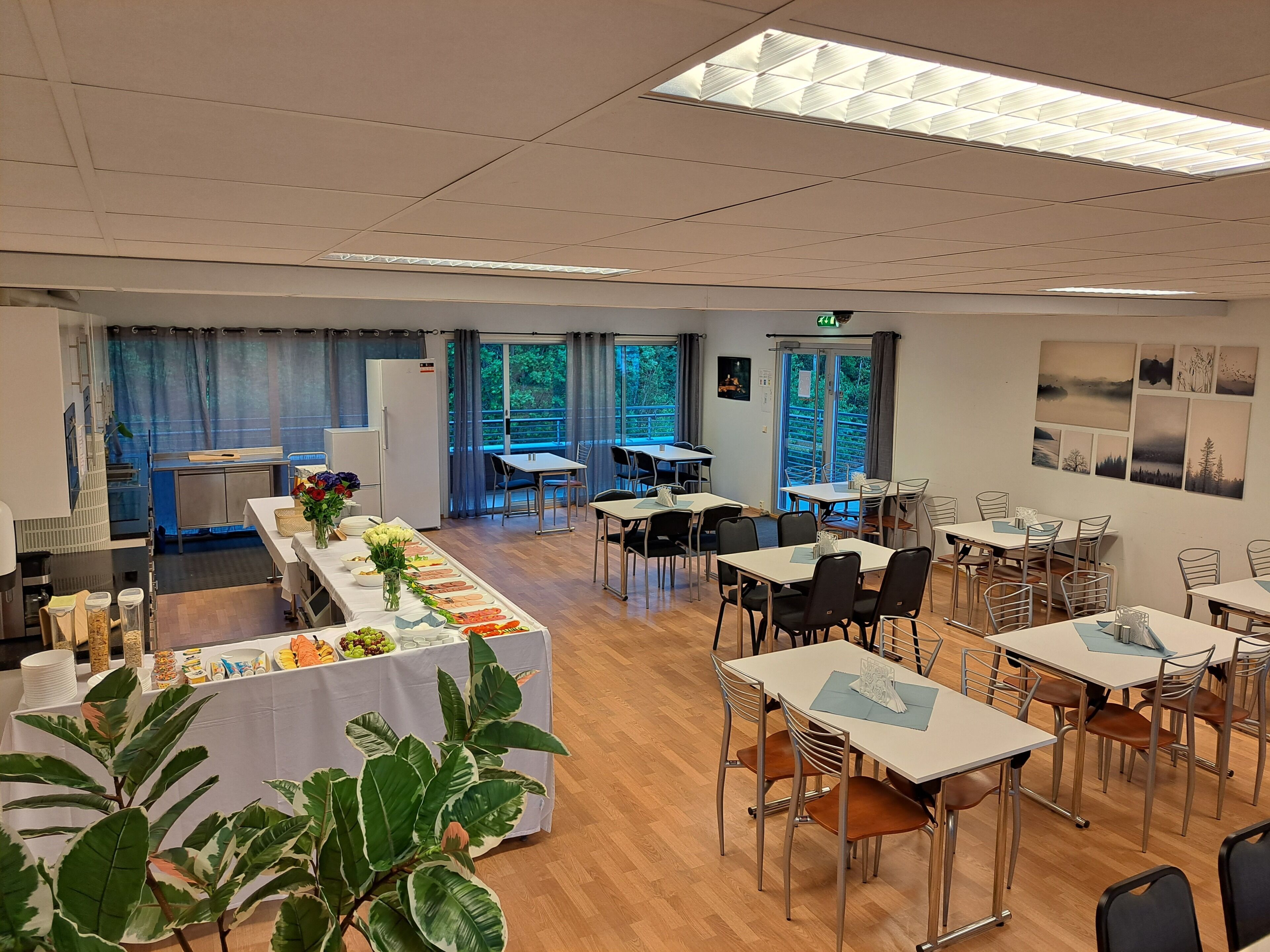 A dining area with tables and chairs, a buffet table with food, and a kitchen area in the background.