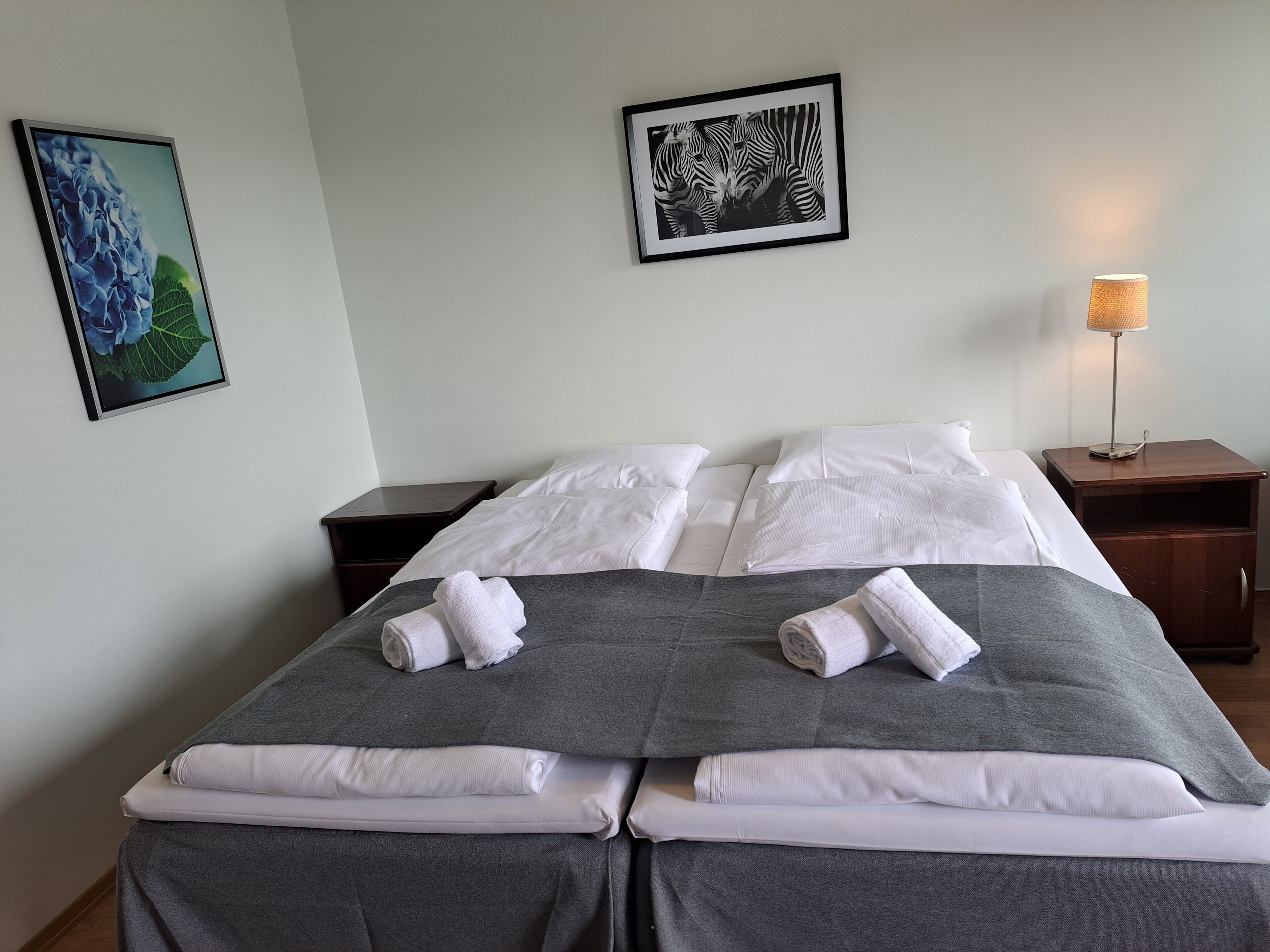 A neatly made double bed with white linens and grey bedding, two nightstands with lamps, and framed artwork on the walls.