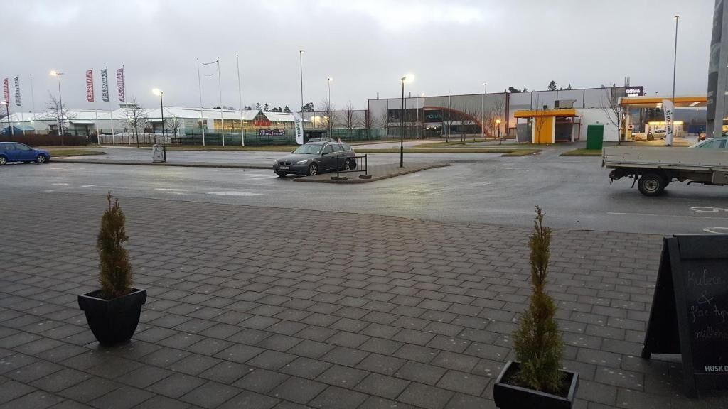 A parking lot with a car and a truck, paved with bricks, and surrounded by buildings with signage.