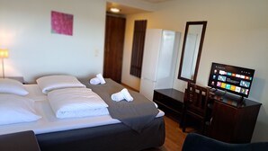 Habitación de hotel con cama, escritorio, silla, televisor y espejo.