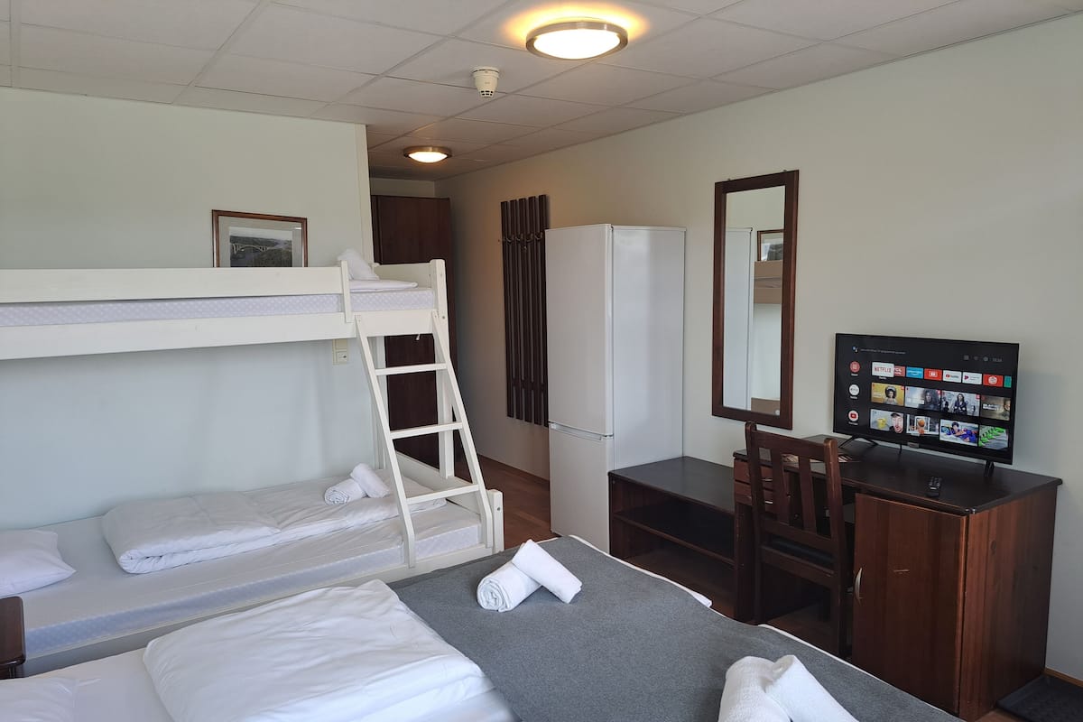 A hotel room with bunk beds, a desk with a computer, a television, and a mirror.