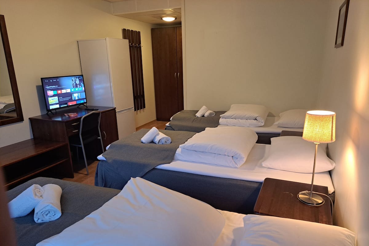 A hotel room with two beds, a desk, a computer, and a lamp.