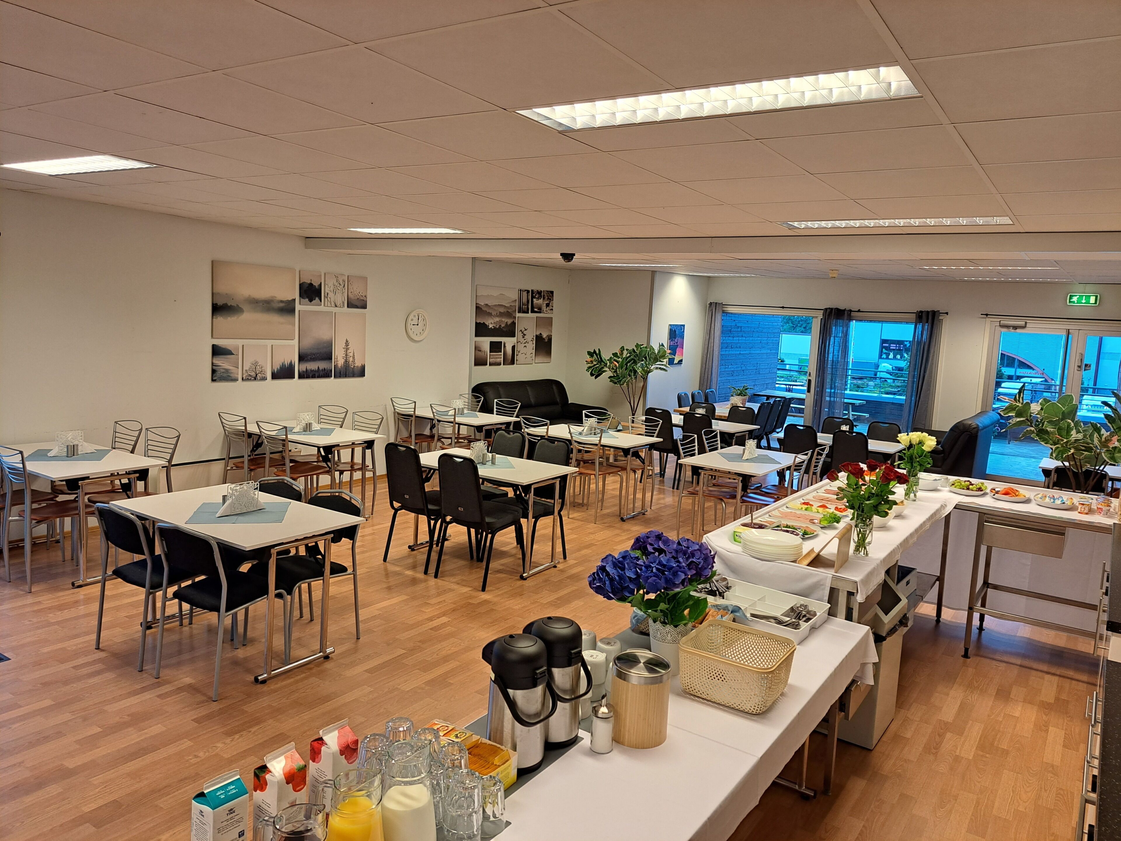 Un grand espace dédié à la salle à manger, avec de nombreuses tables et chaises, un buffet proposant une variété de plats, et une vue sur l’extérieur grâce à de grandes fenêtres.