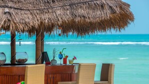 A beach bar with wicker chairs and a thatched roof, overlooking the ocean.