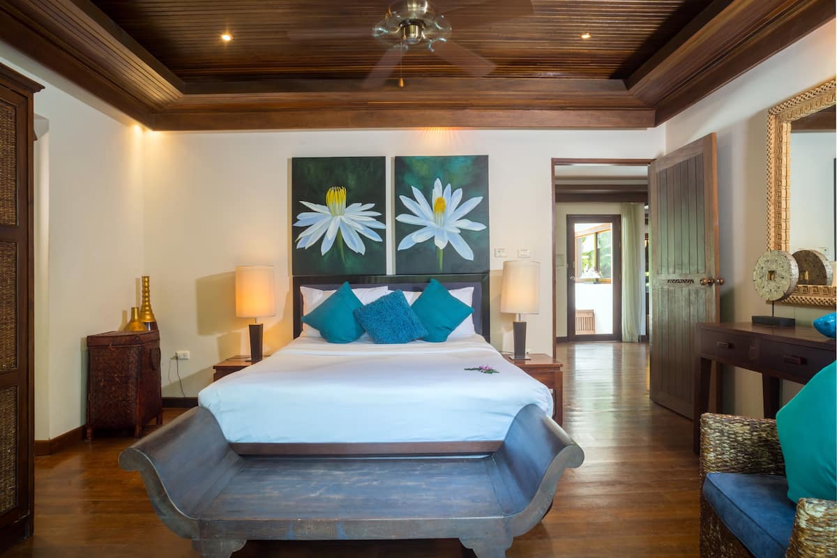 Un dormitorio amplio con una cama grande, dos cuadros colgados en la pared, un banco de madera y techo de madera.