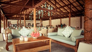 An indoor seating area with wooden tables, cushioned sofas, and hanging pendant lights. - Baan Tawan (Koh Samui)