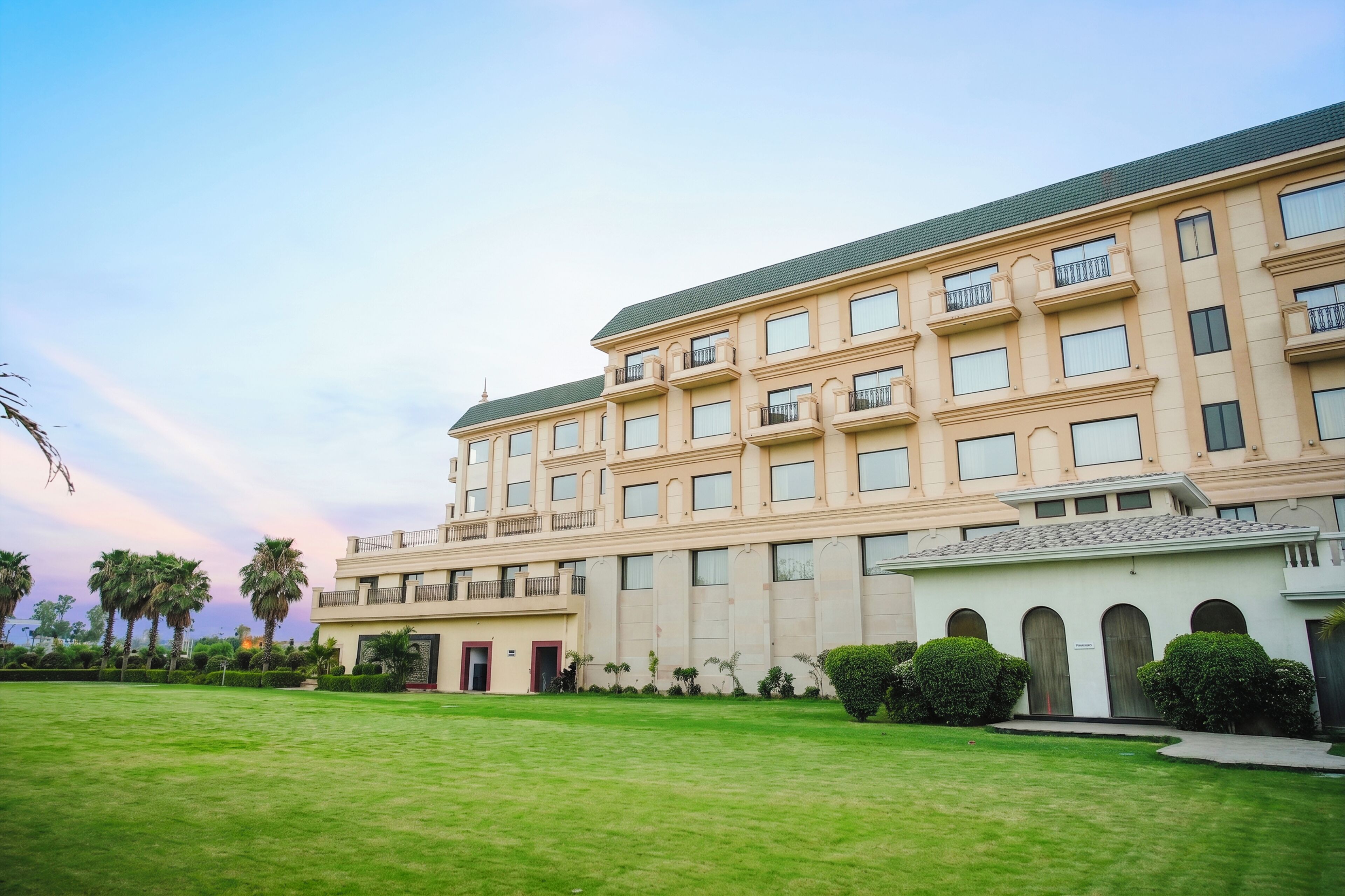 A multi-story hotel with a flat roof, balconies, and a well-maintained lawn.