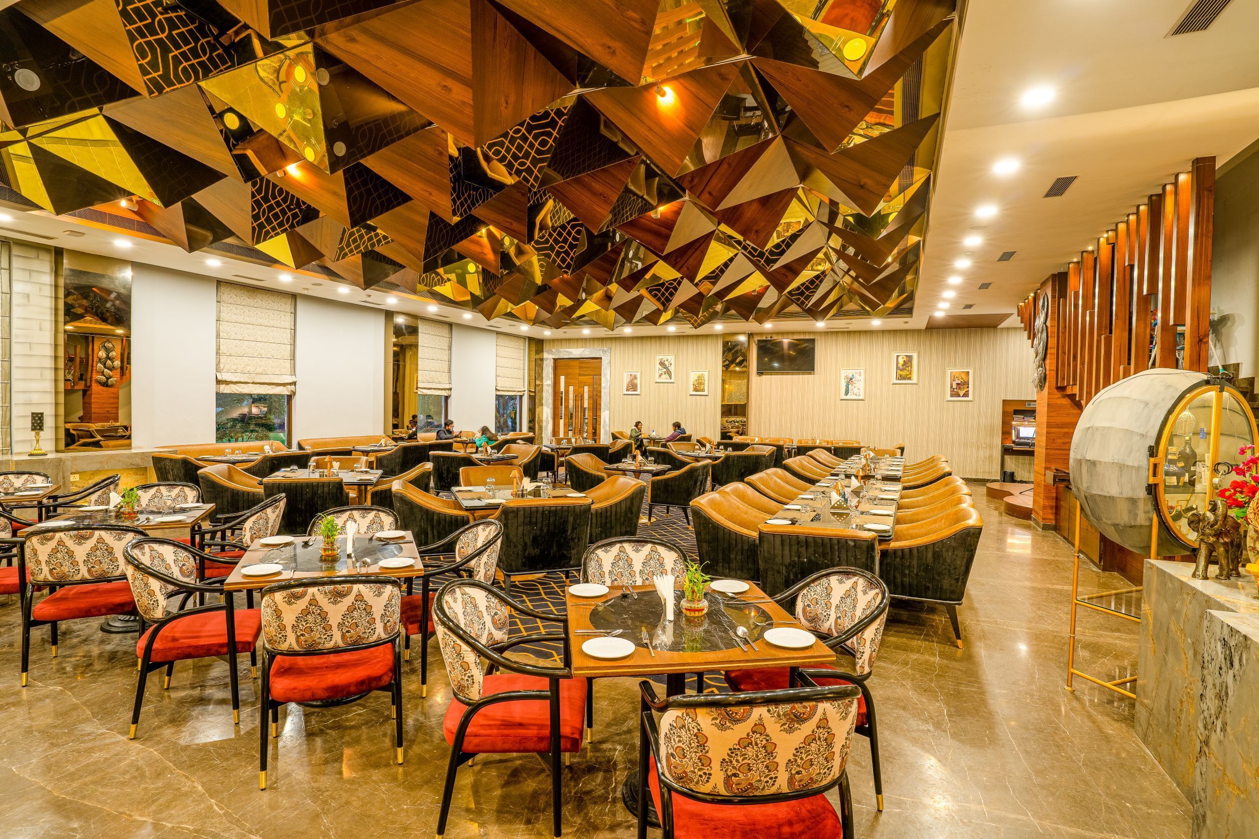 A spacious restaurant with multiple dining areas, wooden ceiling panels, and a marble bar counter.