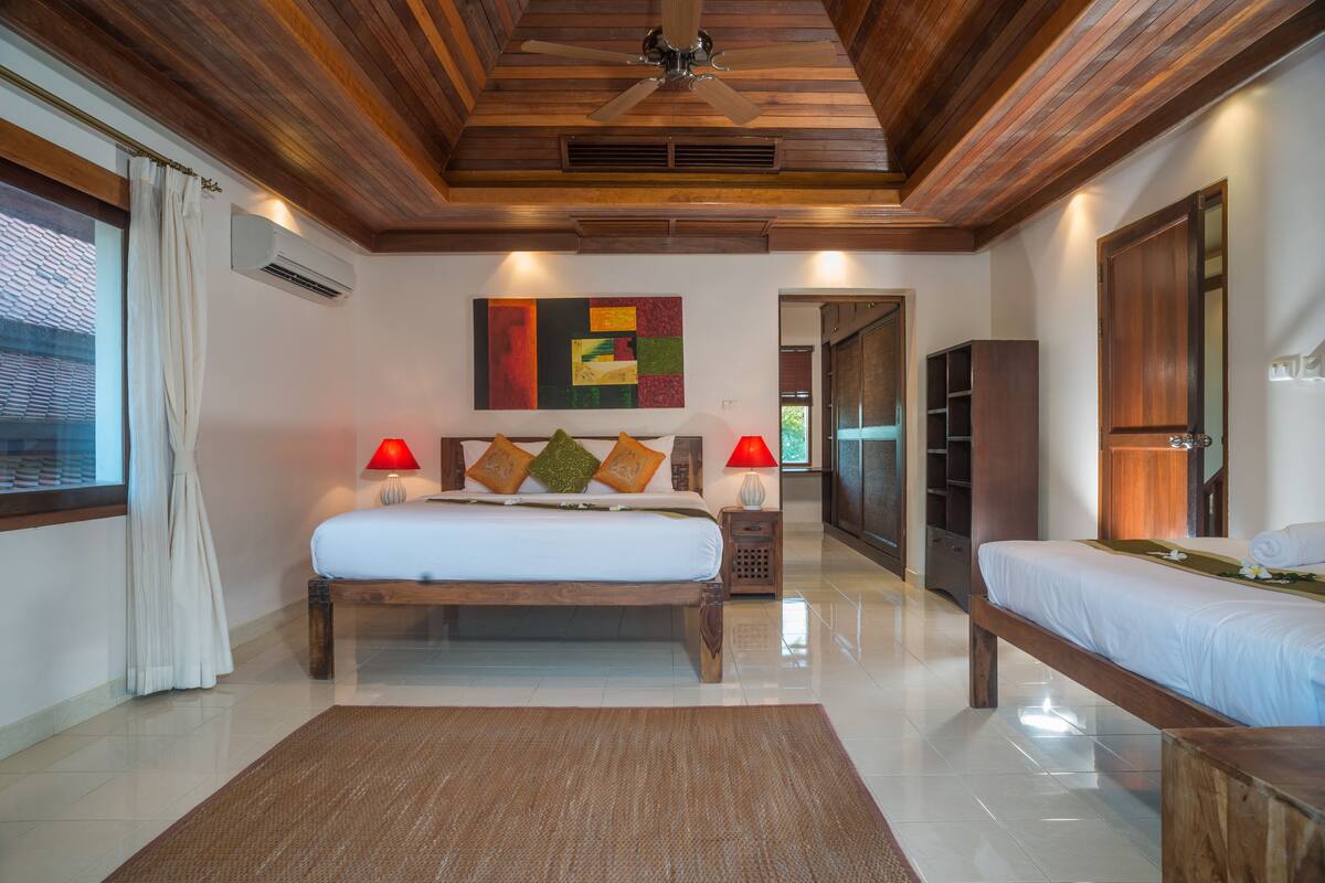 A spacious bedroom with a large bed, a smaller bed, and a wooden ceiling.